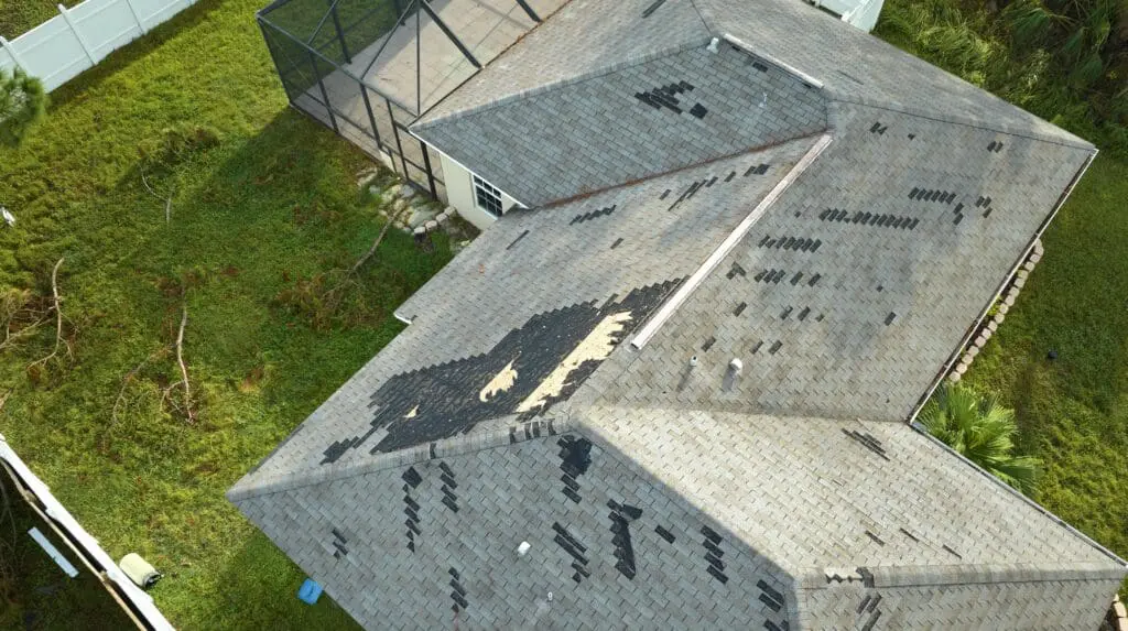 Damaged house roof with missing shingles after hurricane.